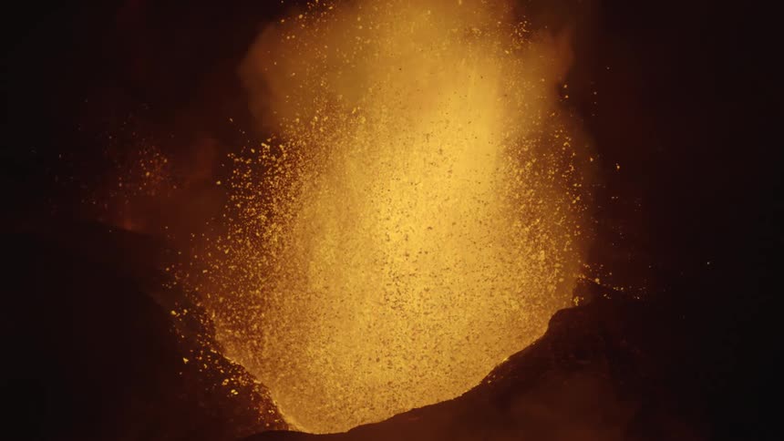 Slow motion volcanic eruption with fountain of orange flames shooting up from mountain at night