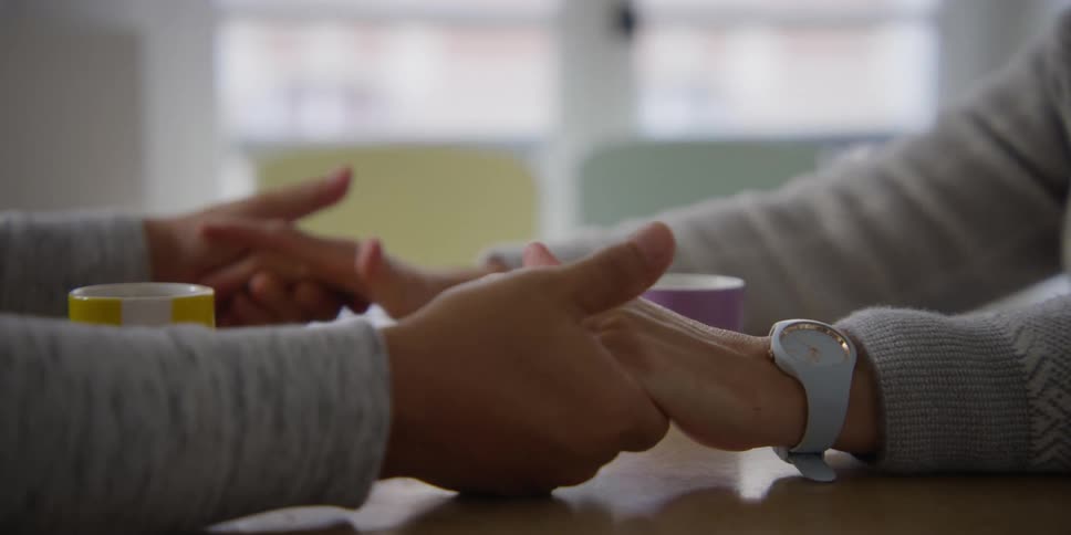 People holding hands sitting at a table drinking coffee
