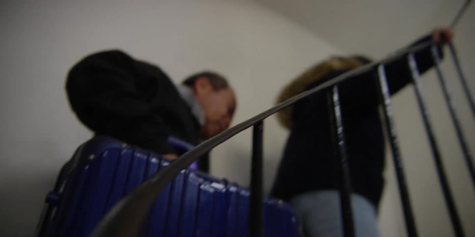 An asian couple climb a staircase with a suitcase