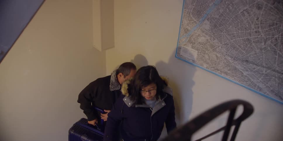 A couple wearing warm clothes are climbing the steps of a small spiral staircase