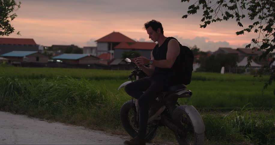 A motorcycle and a person in front of a grassy field and houses at dusk