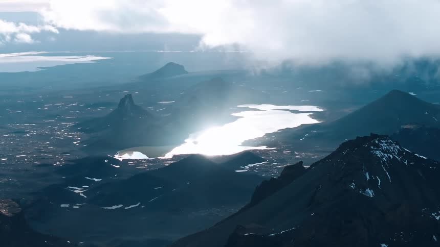 Sunlight glares brightly when reflected from lake bordered by snow dusted mountains