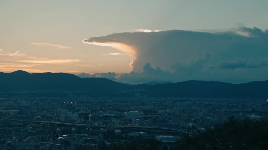 A city below a cloud formation lit by the setting sun
