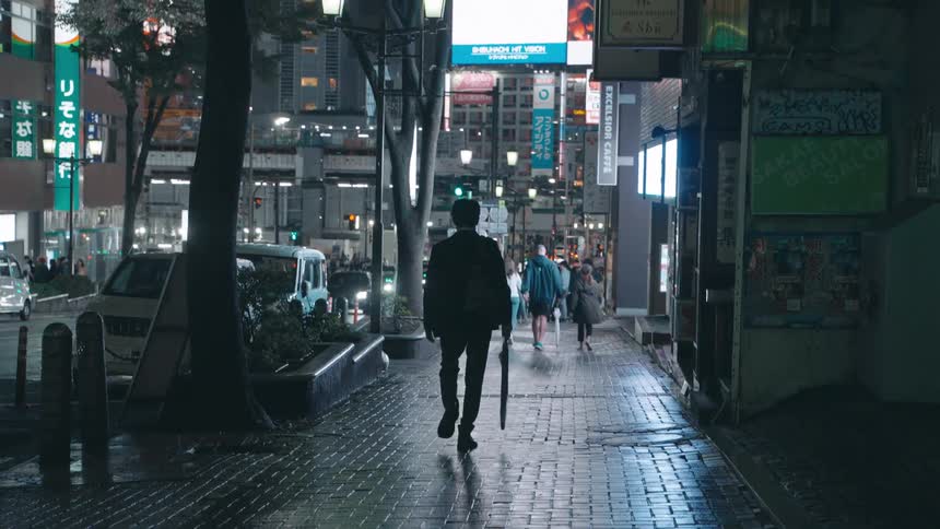 A city lights up the street and buildings as a person walks on a wet sidewalk