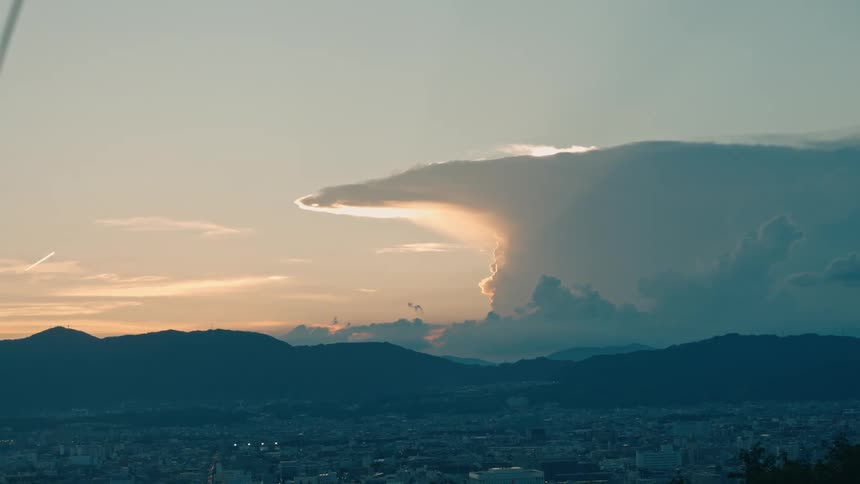 A city below a cloud formation lit by the setting sun