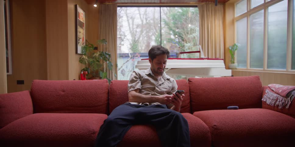 A man sitting on a couch reaches for his smart phone using dance movements