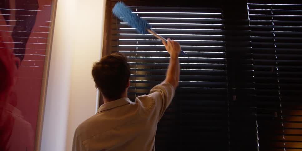A man is dusting his blinds