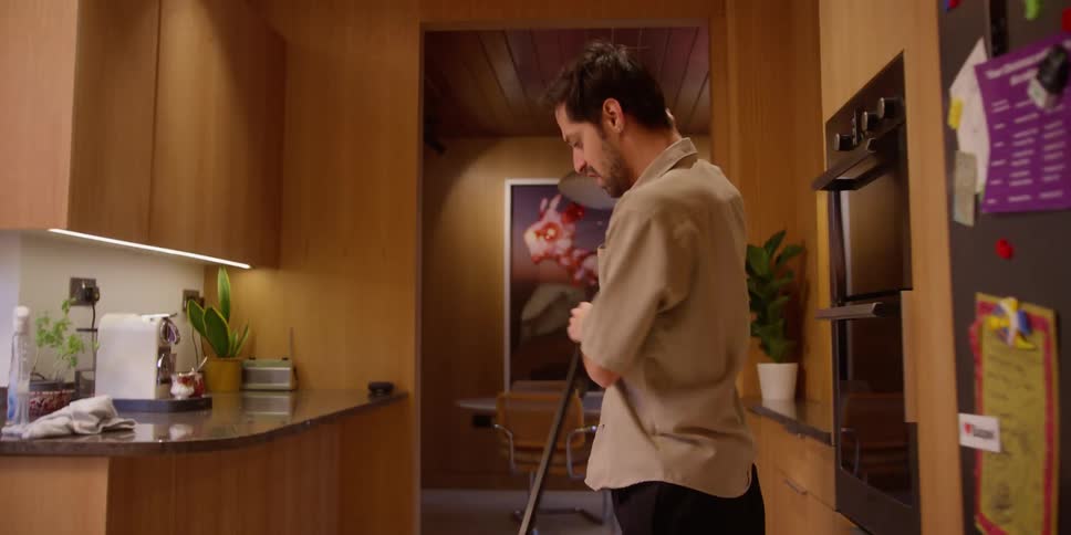 Young man dances while sweeping the floor in the apartment