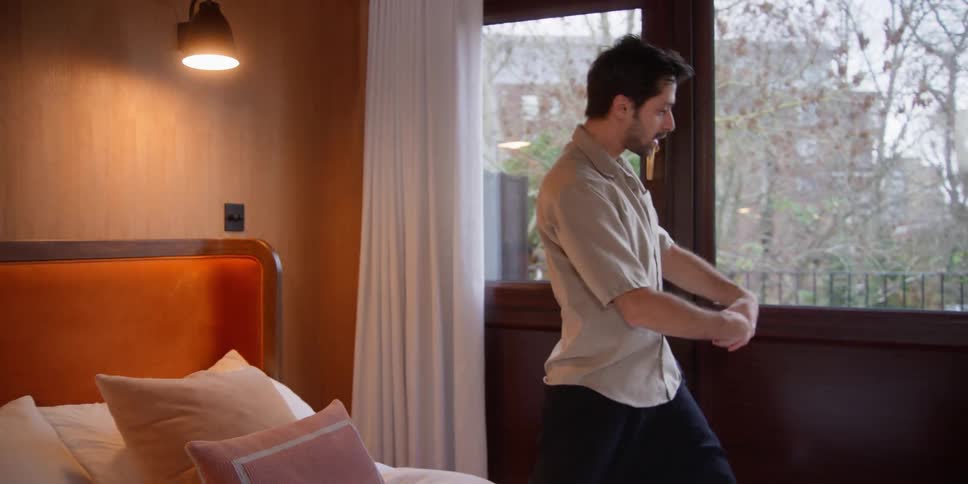 Man meticulously arranging pillows on a bed and dancing