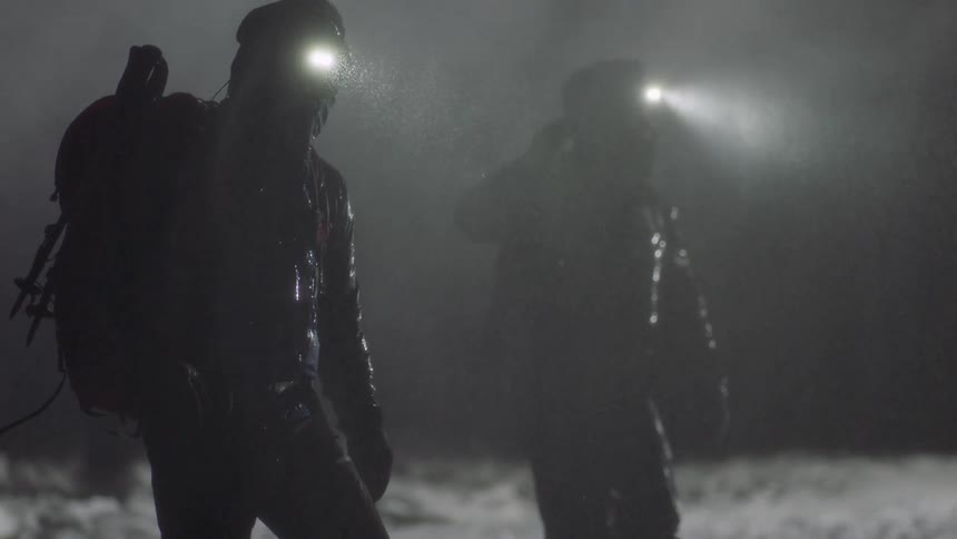 Two people in the middle of a mountain at night on a rainy and snowy day
