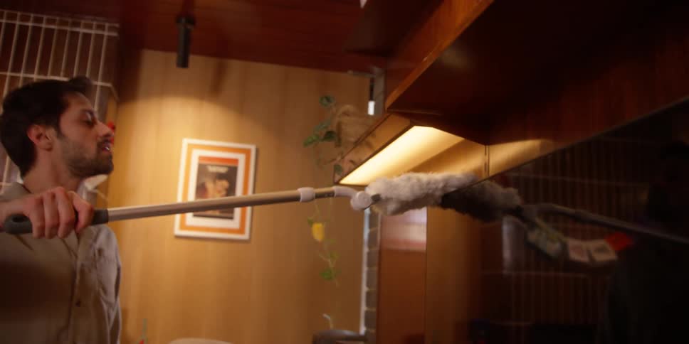 A man uses a duster to clean multiple surfaces inside of a residence