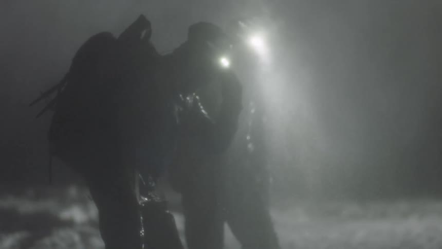 Two men in gears walking with headlights in the rain at night