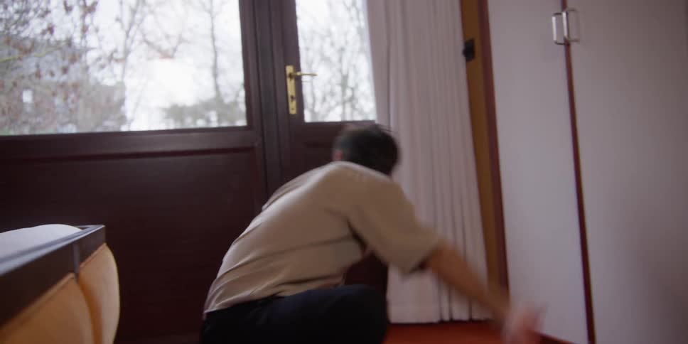 A man cleaning a room interior with a purple utensil while doing dance moves