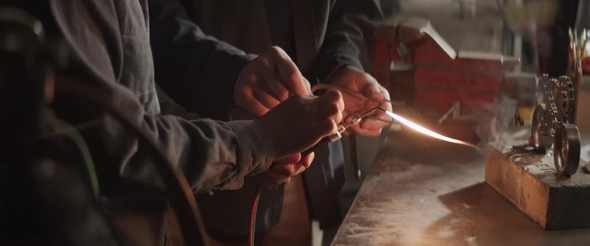 Closeup of the hands of two carpenters welding a piece with a torch