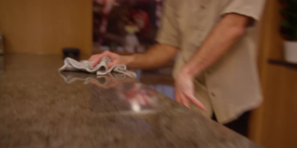 A man is cleaning the surface of a marble table with a cloth and then turns his back and wipes the cloth