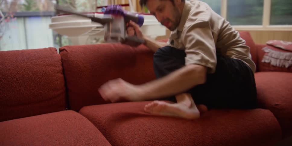 Man vacuuming sofa while dancing