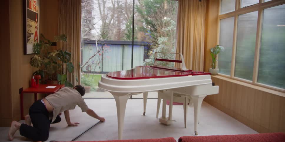 A man performs dance moves while sweeping underneath a piano