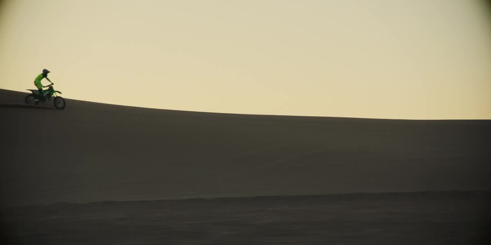 Two people at high speed through the desert dunes performing motocross