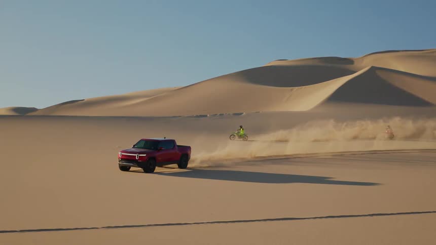 A red pickup truck and two dirt bikes driving on the dunes of a desert under a blue sky