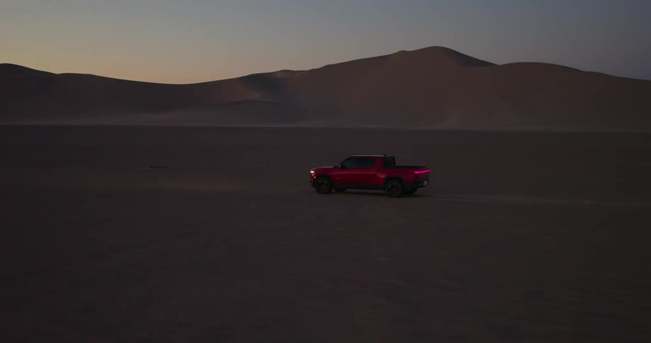 A red truck driving in a desert with several dunes in the background