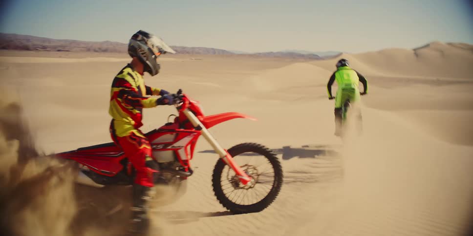Two people with their own motocross bikes speeding through the desert dunes