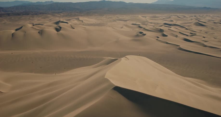 A desert region with huge sand dunes and on the horizon there are large mountains