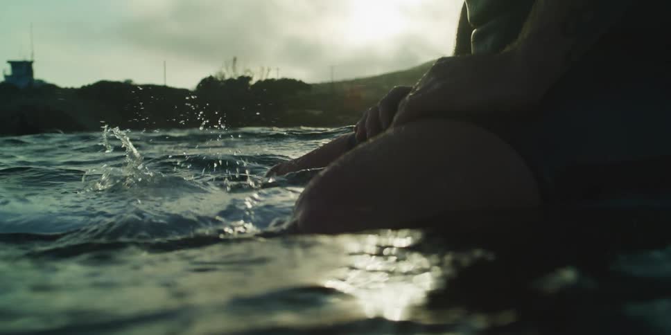 A person sitting on a board in the water and their feet are moving underwater