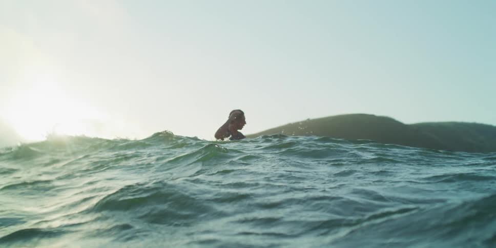 A man is surfing a sea wave and on the horizon there are mountains
