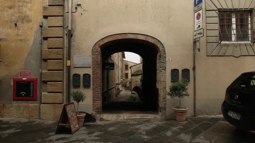 An arch leads down a narrow alleyway in an old city during daylight