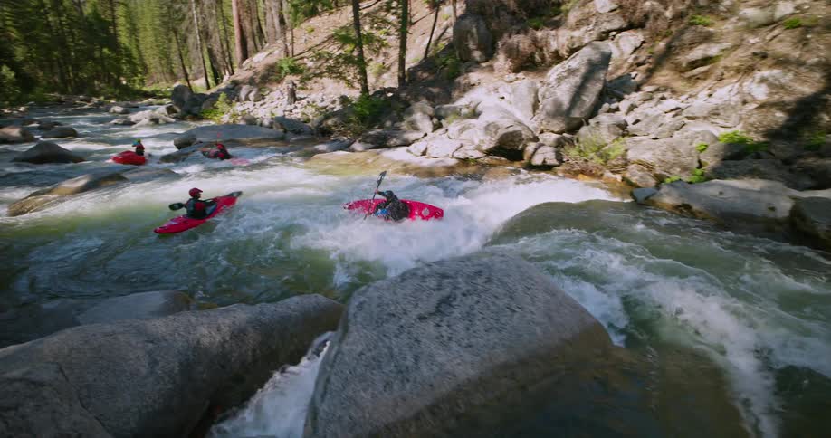 People kayaking down a rapid river surrounded by rocks and trees
