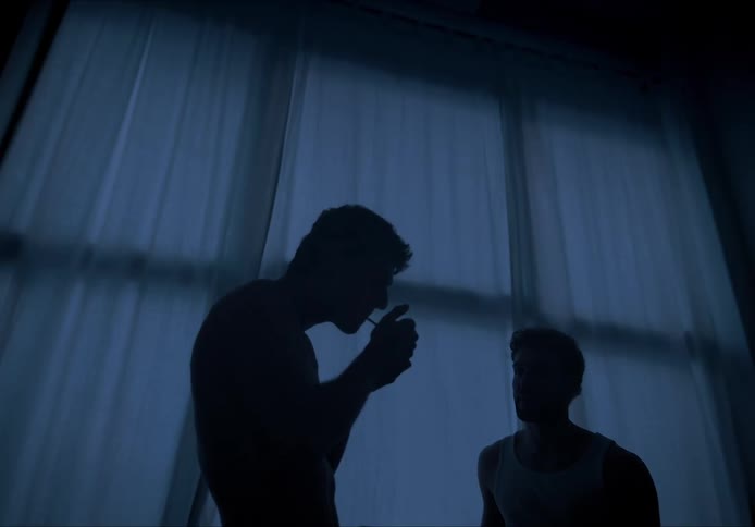 Two men sitting in a dark room smoking cigarettes