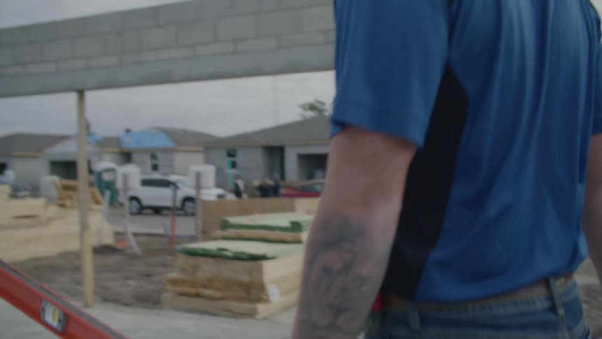 A construction worker carries a level through an incomplete building