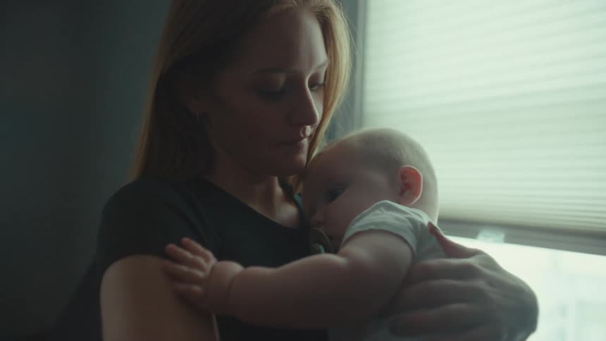 A mother is holding her small baby on her lap and stroking his back