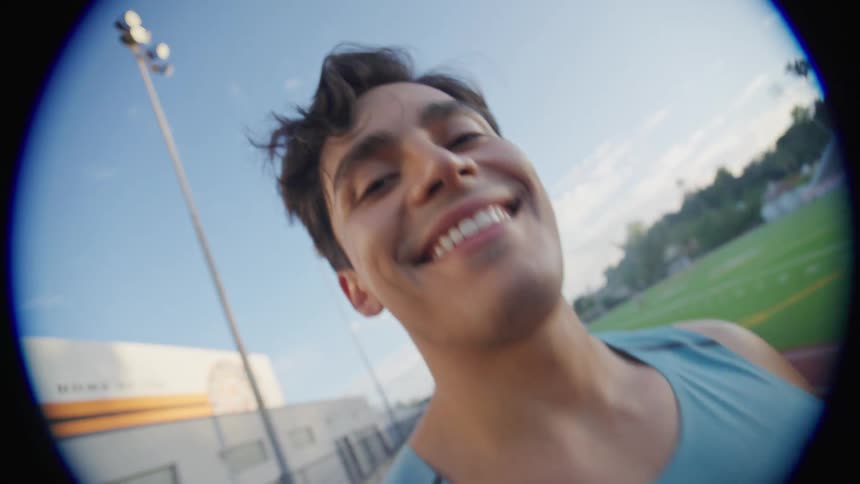 A young man is smiling in a field with a running track