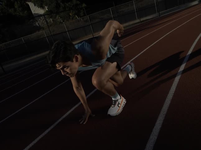 Male athlete taking off from runners starting position on an outdoor track at night in slow motion