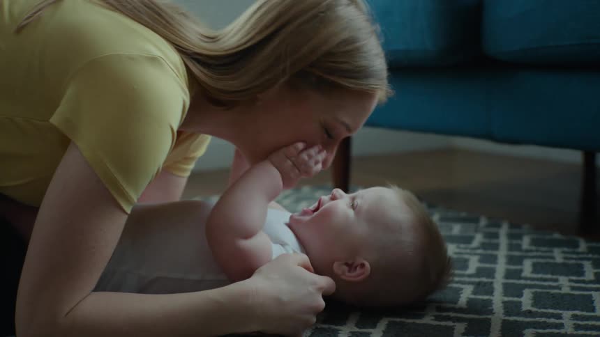 A young mother laughs and plays with her baby while lying on the floor