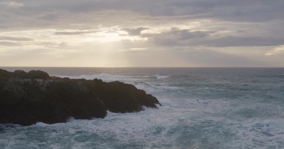 Sea waves break on the mountain shore during sunset
