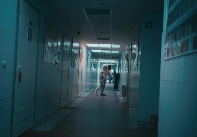 A man with a cast and crutches stands in a dark hospital hallway