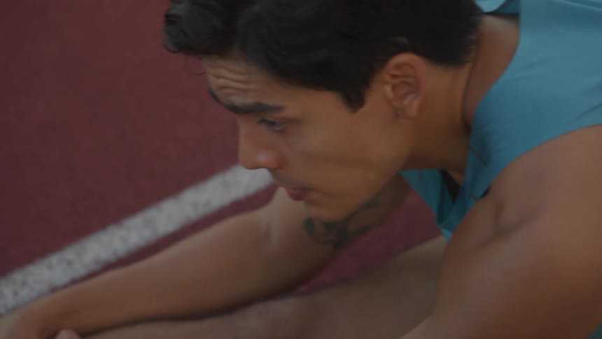 Man sitting on an athletics court stretching his legs