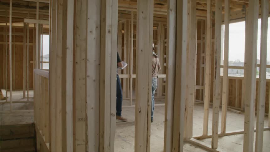 Two men with protective helmets walking inside a construction site and talking
