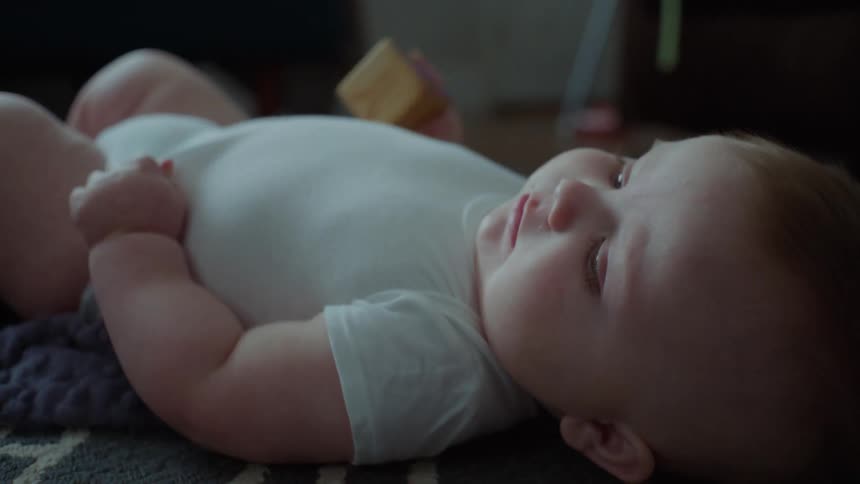 A baby plays with a block while lying on the floor