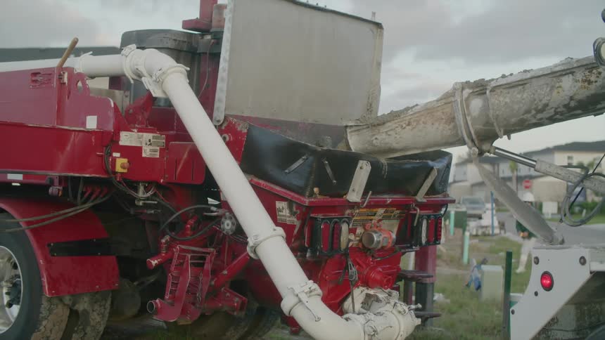 A concrete pump truck pouring its contents inside another truck