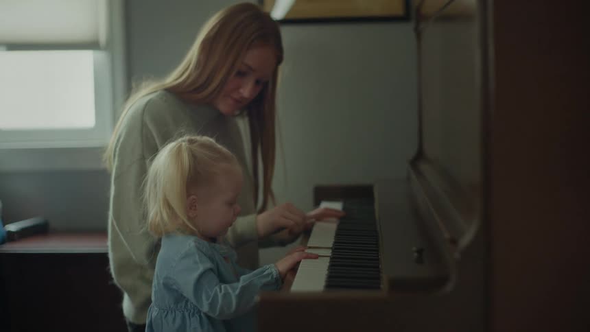 A mother shows her toddler daughter how to play a piano