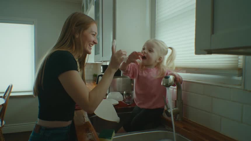 A mother and daughter laugh at the kitchen sink