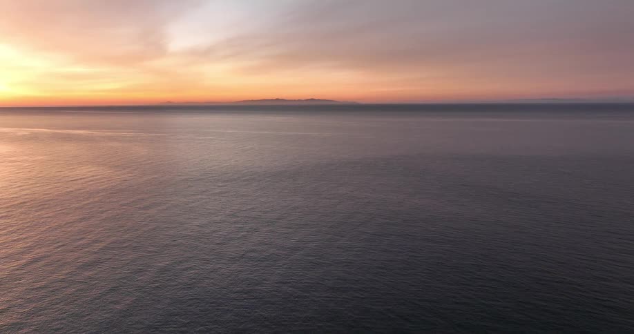An aerial view of a calm sea that goes all the way to the horizon and there is an orange sky