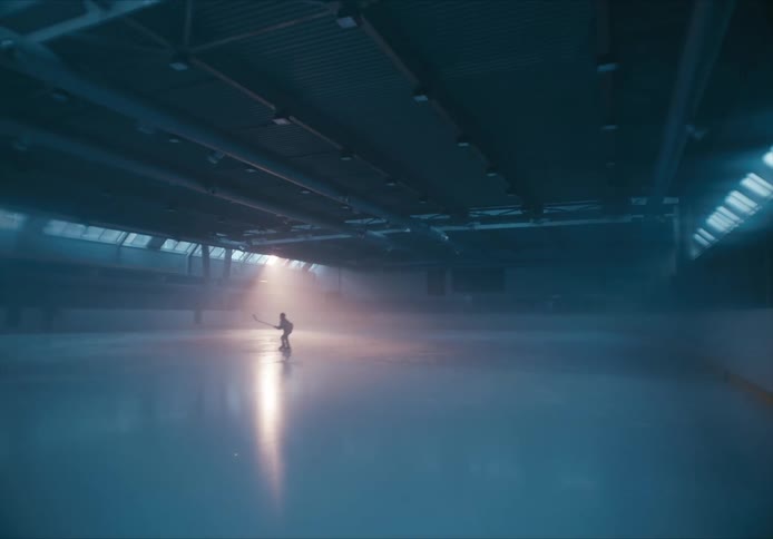 Ice hockey player skates circle on a dimly lit indoor ice rink