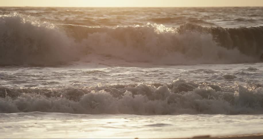 Angry waves crash onto the beach during sunset