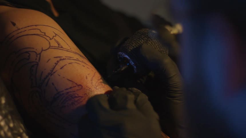 Tattoo artist wears gloves while tattooing face onto clients arm
