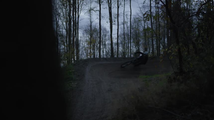 A cyclist rides a mountain bike on a curved trail through the woods