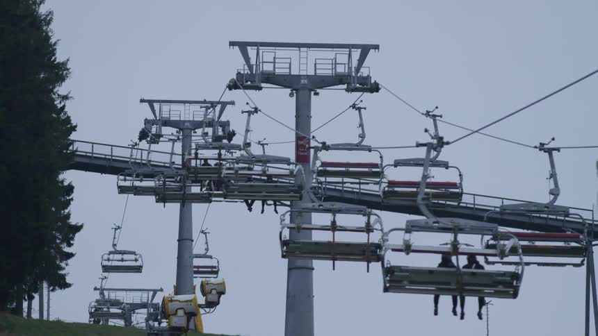 Two passengers sitting on a ski lift ascending a green hill